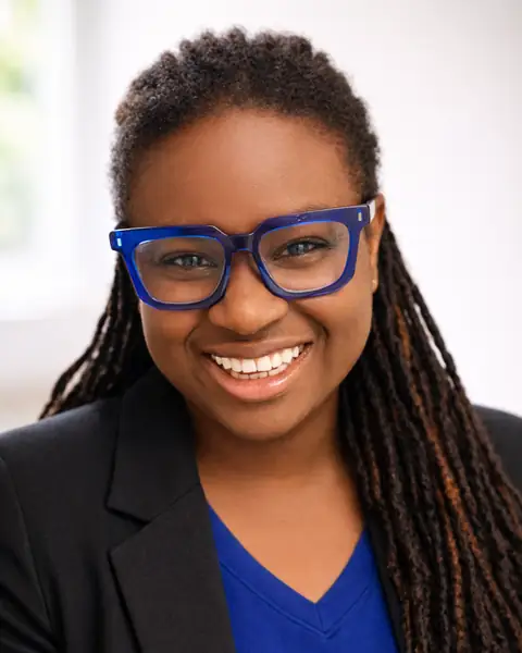 Kamla A. Williams, MA, RSW, smiling in blue glasses and a dark blazer